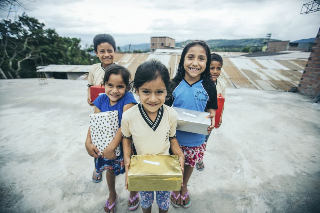 A group of children stand, facing the camera, holding wrapped Christmas gifts.